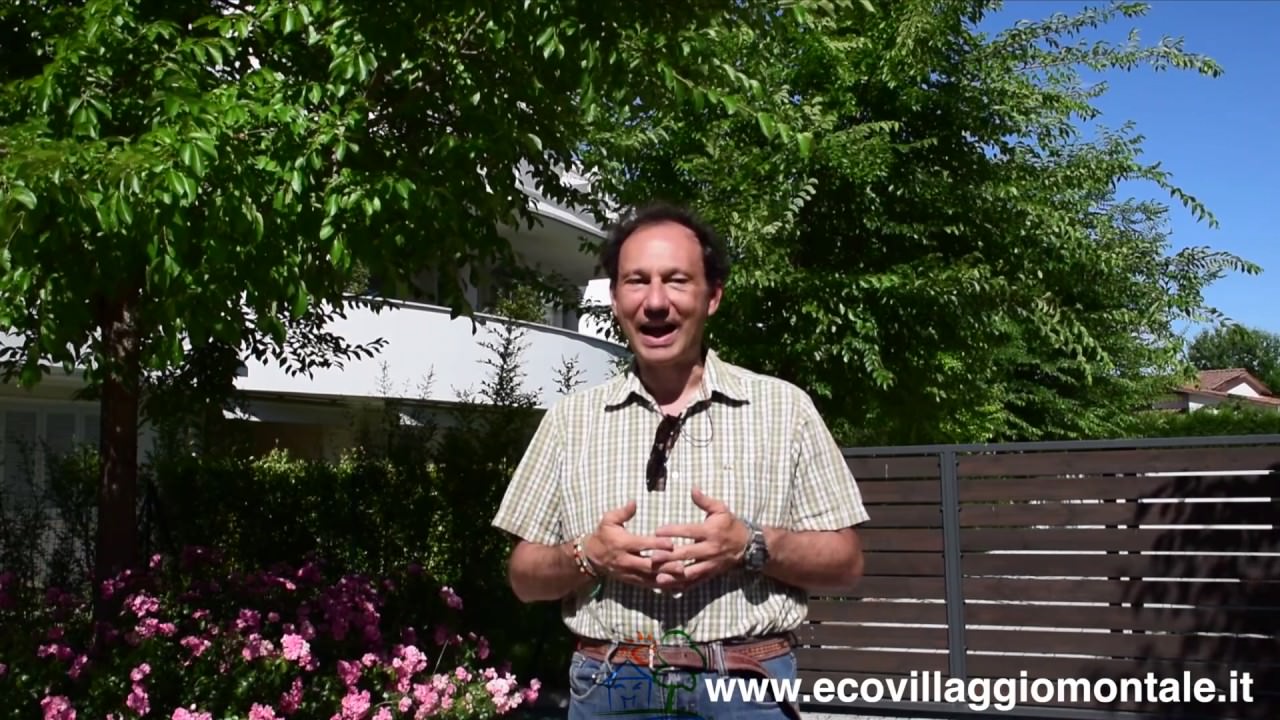 Uomo sorridente spiega come calcolare le emissioni di CO2, circondato da piante e fiori in un ambiente naturale e luminoso.