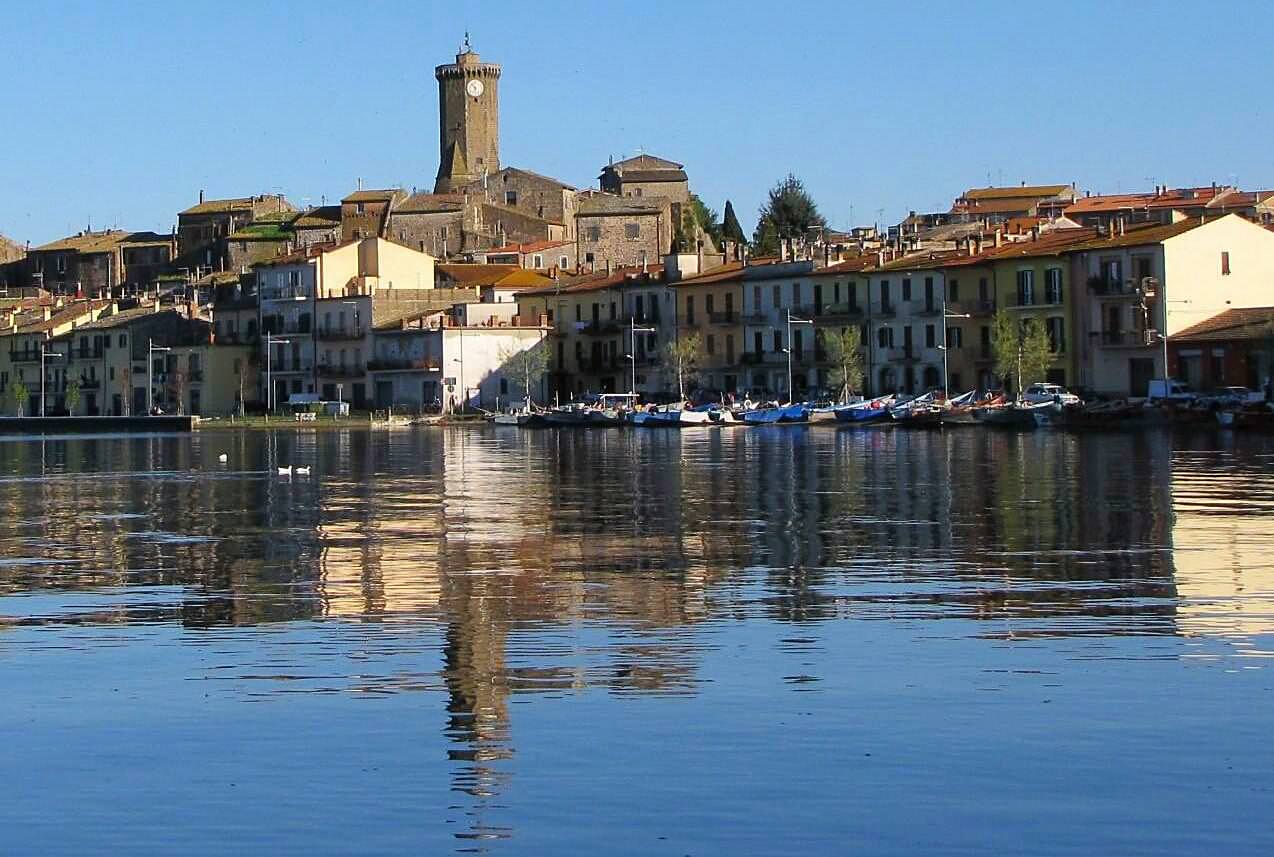 Panorama del lago di Bolsena con il borgo di Marta, incantevoli case colorate e il caratteristico campanile che si riflette nell'acqua.