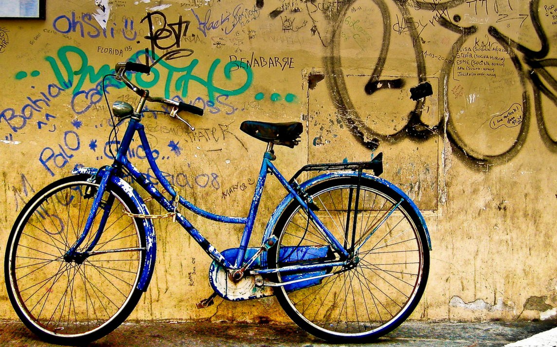 Bici abbandonata restaurata, appoggiata a un muro graffiti, simbolo di riutilizzo e sostenibilità nel progetto RiCiclo per biciclette.