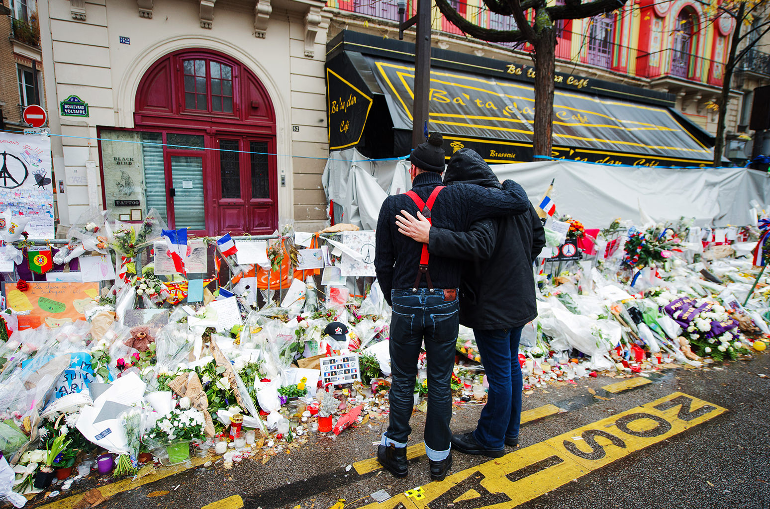 Due uomini abbracciati davanti al memoriale del Bataclan a Parigi, adornato di fiori e messaggi, commemorando le vittime del 2015.
