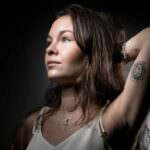 Ritratto di una donna con un tatuaggio commemorativo e sguardo significativo, simbolo di resilienza e memoria due anni dopo il Bataclan.