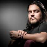 Uomo con capelli lunghi e tatuaggio visibile sul braccio, in un'illuminazione drammatica, riflette sul significato del ricordo del Bataclan.