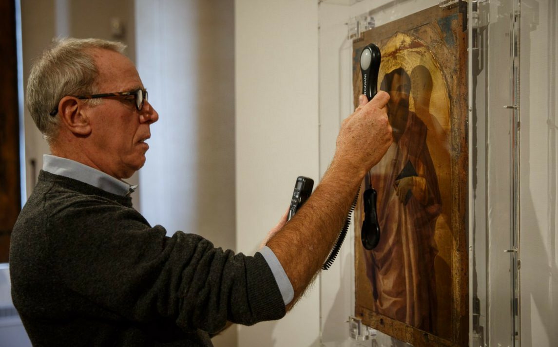 Un visitatore osserva attentamente un’opera d’arte al museo, esplorando dettagli attraverso un telefono informativo nella mostra a Roma.