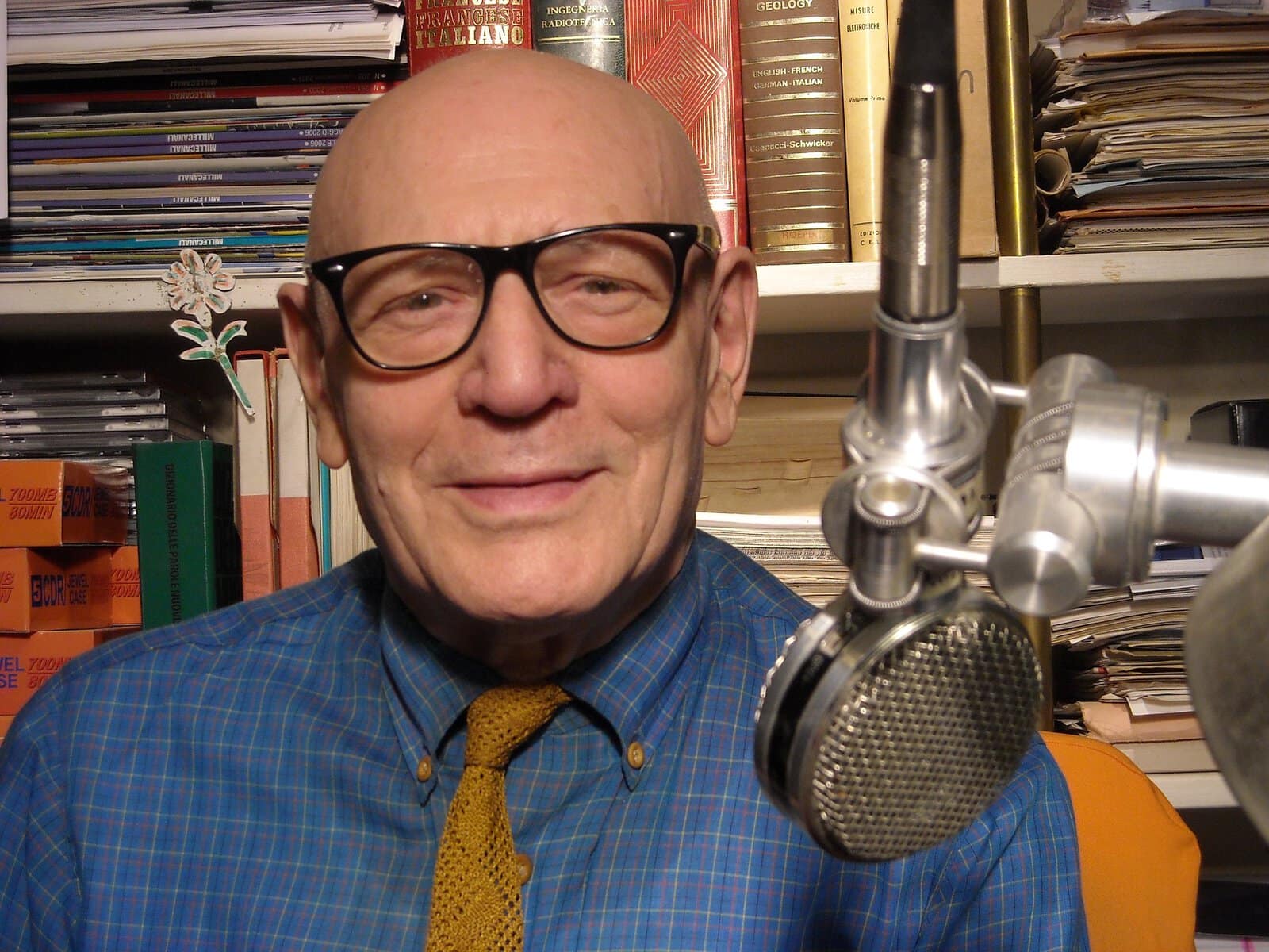 Mario Albanesi, volto storico di TeleAmbiente, in un momento di riflessione accanto al microfono, simbolo della sua dedizione all'informazione.