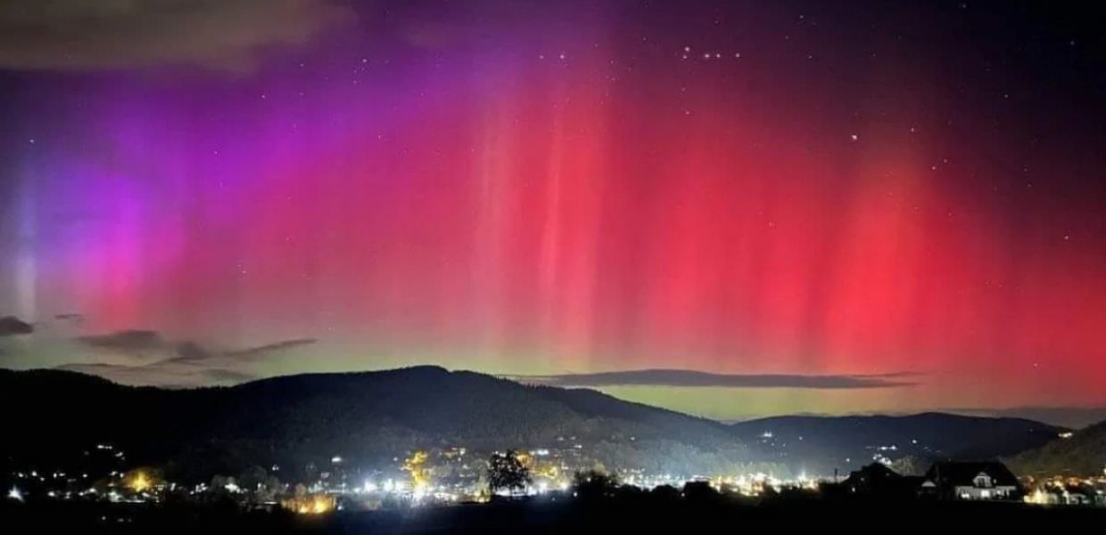 Testo alternativo: Immagine dell'aurora boreale in Italia, con sfumature violetto e rosso sullo sfondo di un paesaggio montano illuminato.