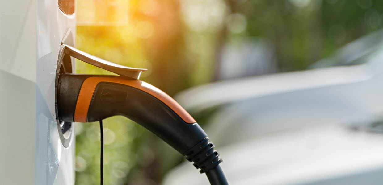 Caricatore di un'auto elettrica in un'area di sosta soleggiata, simbolo dell'interesse crescente degli italiani per la mobilità sostenibile.