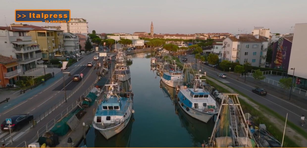 Vista panoramica di un canale costiero con pescherecci e edifici, evidenziando l'integrazione tra economia del mare e sostenibilità ambientale.