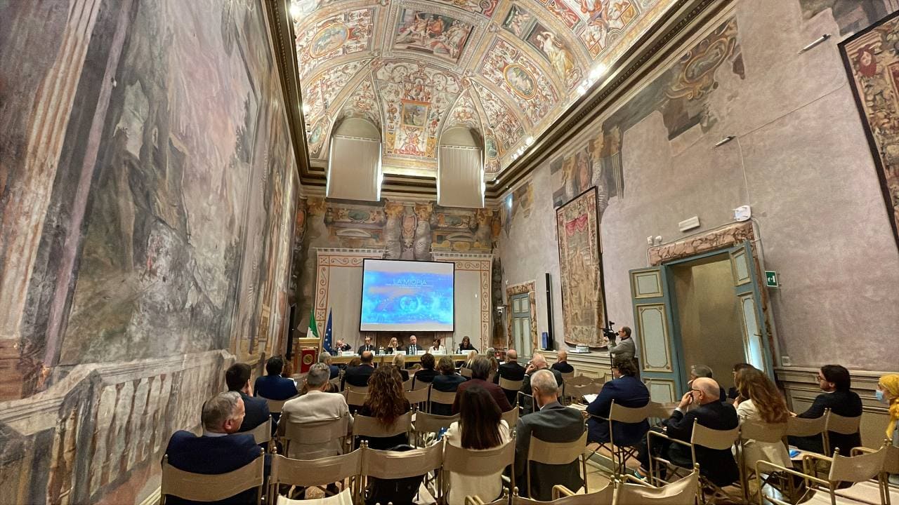 Convegno al Senato sulla miopia, con relatori e pubblico in una suggestiva sala affrescata, durante la presentazione di strategie innovative.