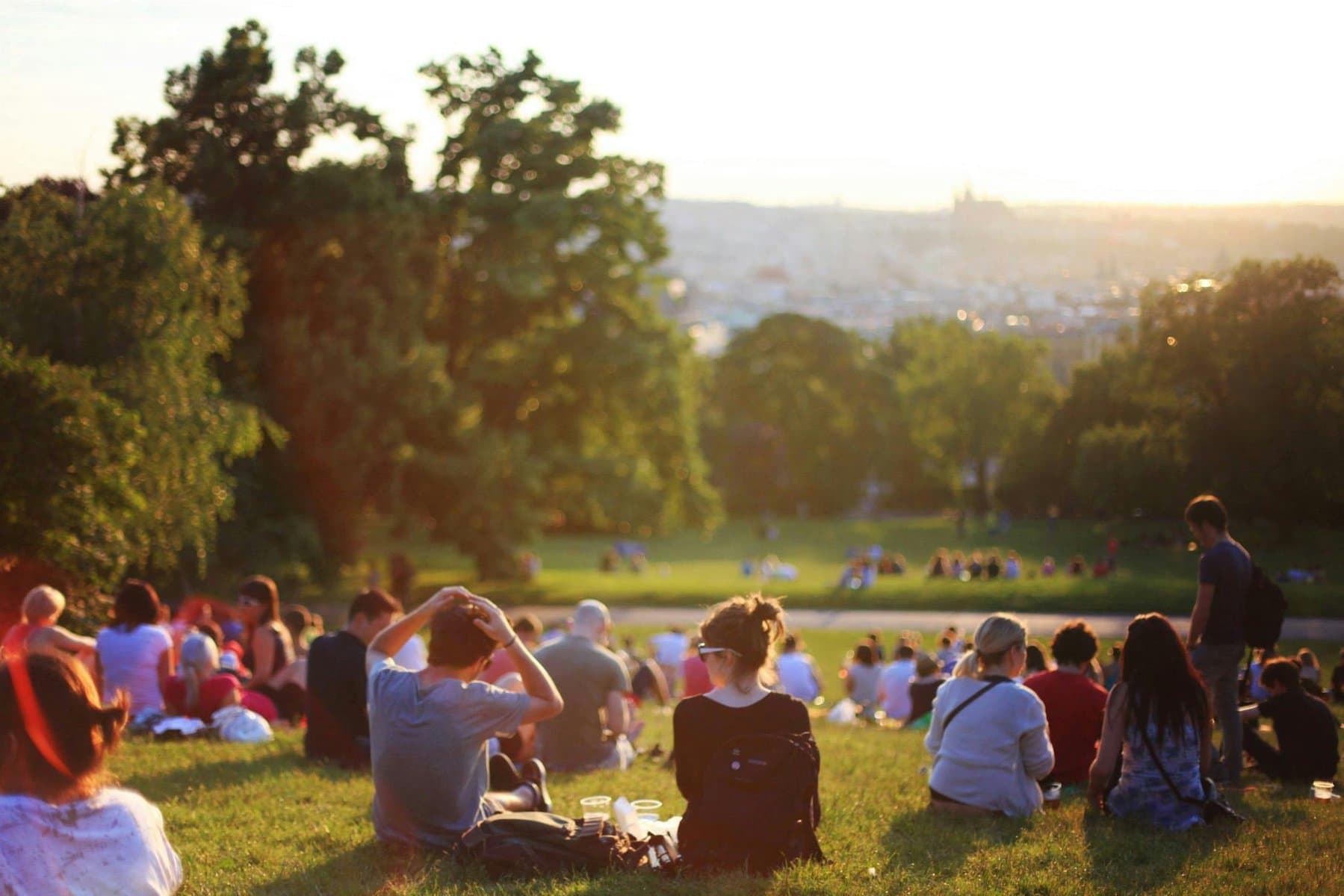 Persone che si rilassano in un parco urbano al tramonto, evidenziando l'importanza delle aree verdi per la salute e il benessere in città.