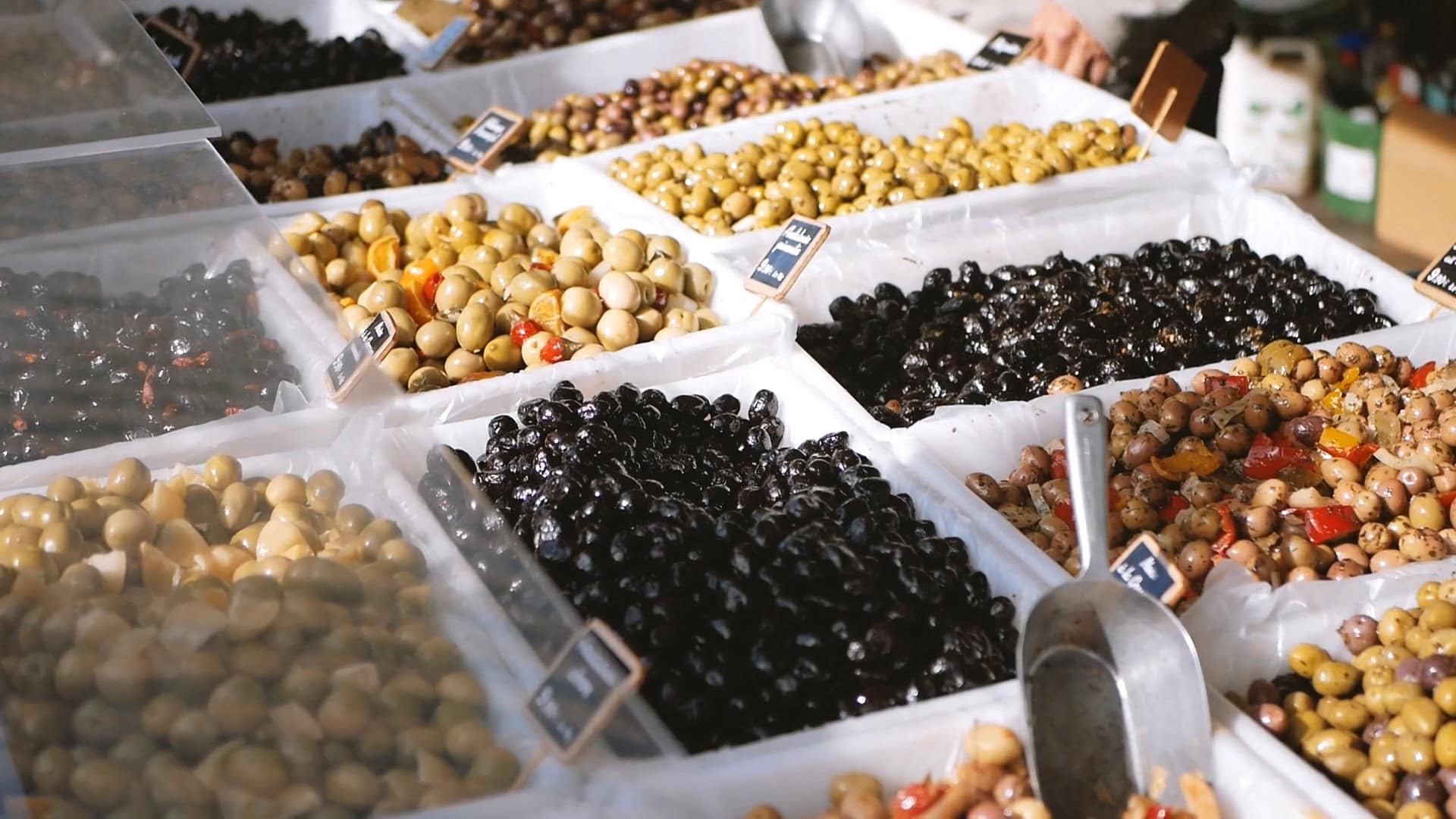 Vassoi di olive di diverse varietà in un mercato, evidenziando la ricchezza dell'olio d'oliva e del patrimonio culinario europeo.