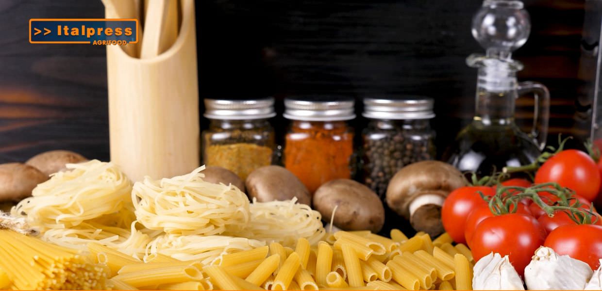 Ingredienti freschi per la pasta: pomodori, funghi, spezie, olio d'oliva e vari tipi di pasta su un tavolo di legno, rappresentando la cucina italiana.