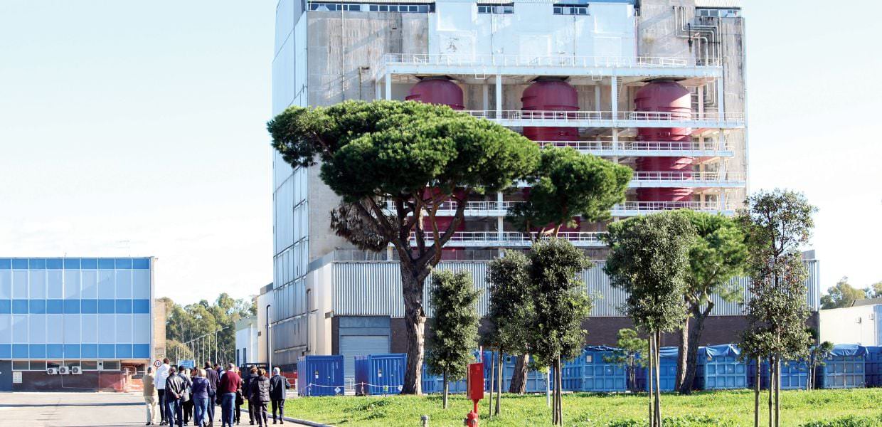 Cantiere di Sogin alla Centrale di Latina per lo smantellamento dei sei boilers, con operai e edifici industriali sullo sfondo.