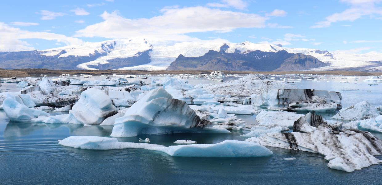 Immagine di iceberg galleggianti in un lago con montagne sullo sfondo, simbolo della crisi climatica e dei costi economici in Italia.