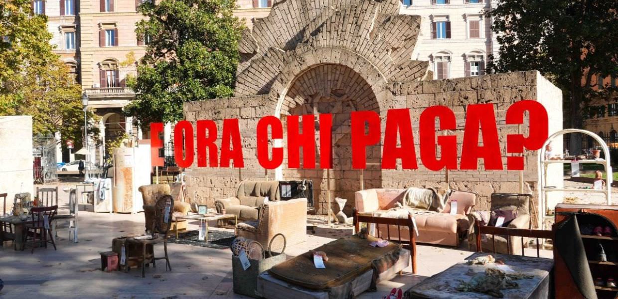 Immagine dell'installazione artistica di Greenpeace a Roma, che evidenzia i danni della crisi climatica con arredi danneggiati e il messaggio provocatorio Ora chi paga?.