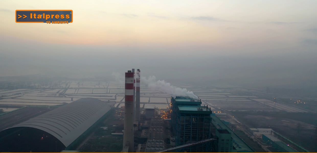 Fumi e emissioni da una centrale elettrica, con sfondo di un paesaggio industriale, simbolo delle sfide ambientali legate alle fonti fossili.