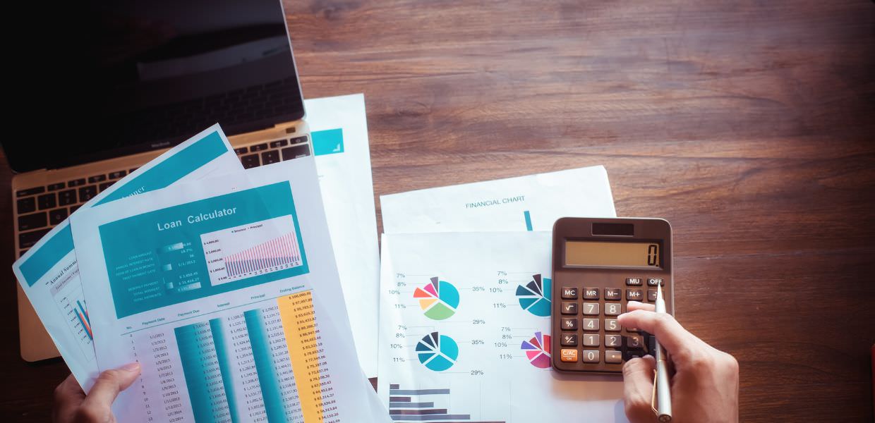 Calcolatrice su tavolo con fogli di analisi finanziaria e grafici, utile per affrontare l'aumento delle bollette e pianificare risparmi.