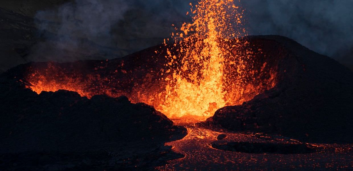 Eruzione di un vulcano in Islanda, con lava incandescente che fluisce, simbolo dell'uso del calore del magma per riscaldamento sostenibile.