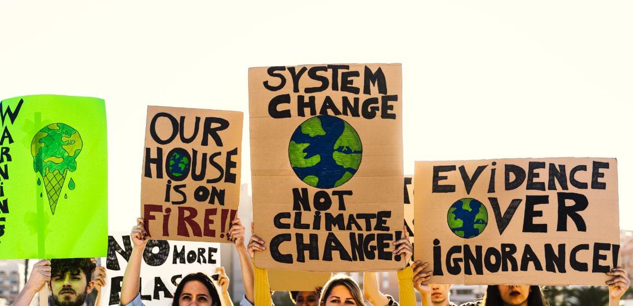 Manifestazione con cartelli che denunciano la crisi climatica, evidenziando call-to-action per il cambiamento sistemico e la necessità di azione.