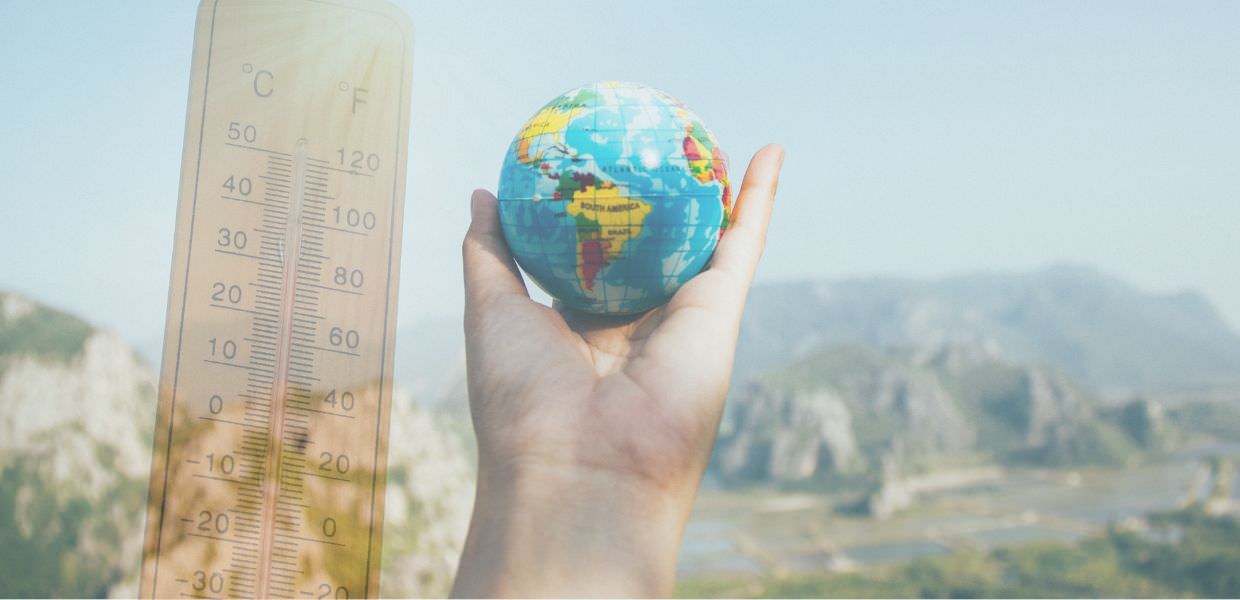 Testo alternativo: Mano che tiene un globo terrestre con termometro che segna temperature elevate, simbolo del riscaldamento globale verso +2,7°C.