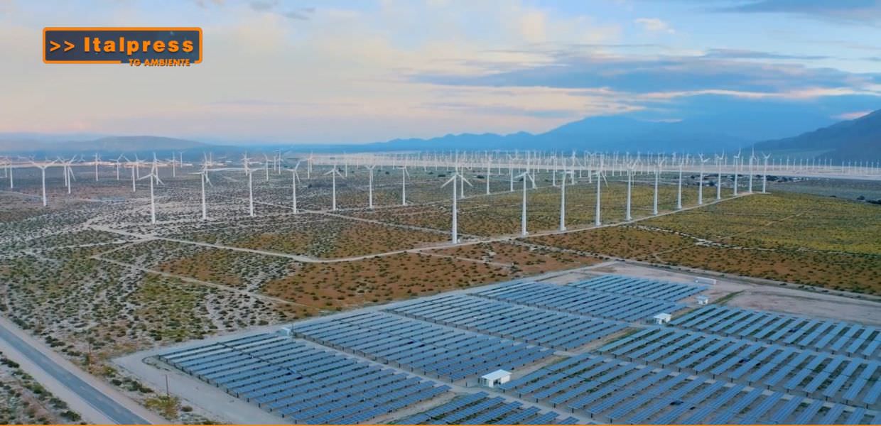 Immagine di un vasto campo di pannelli solari e turbine eoliche, simbolo della transizione energetica e delle rinnovabili per combattere la crisi climatica.