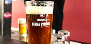Bicchiere di birra scura con logo della Fabbrica Birra Perugia, simbolo dei 150 anni di tradizione birraia in Umbria.