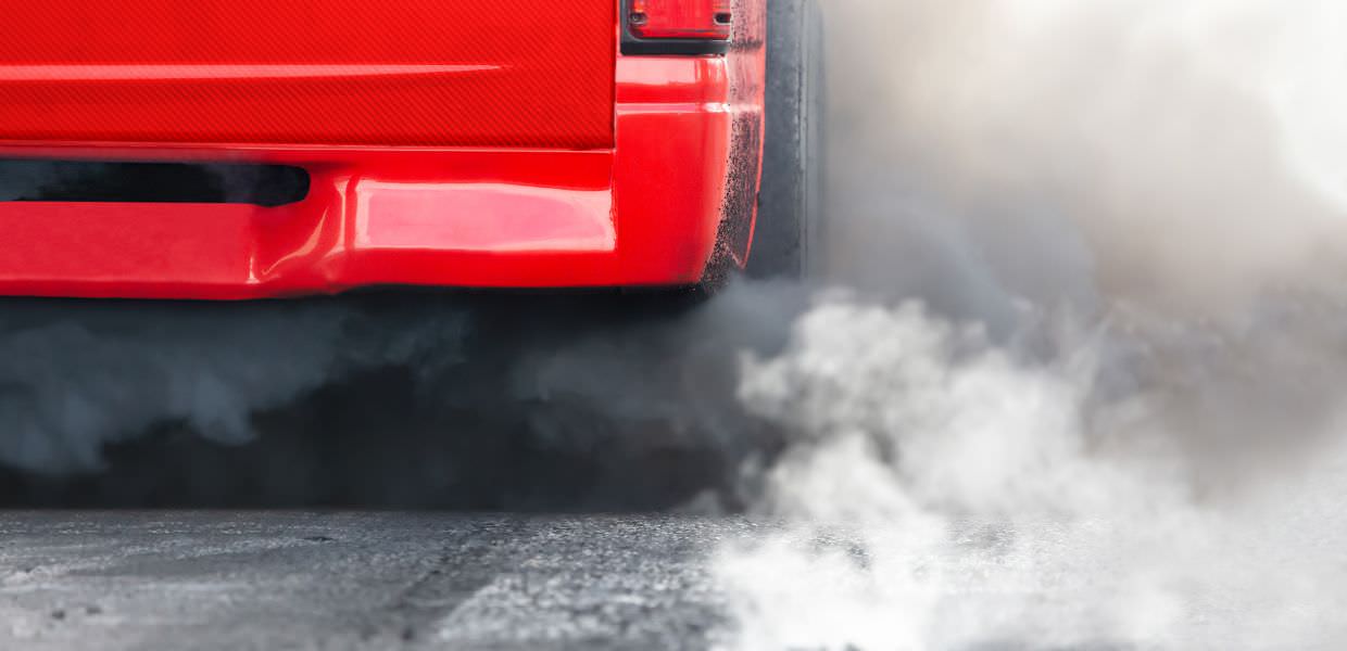 Emissioni di fumi nocivi da un'auto rossa, simbolo dell'inquinamento atmosferico in 25 città italiane fuori legge.